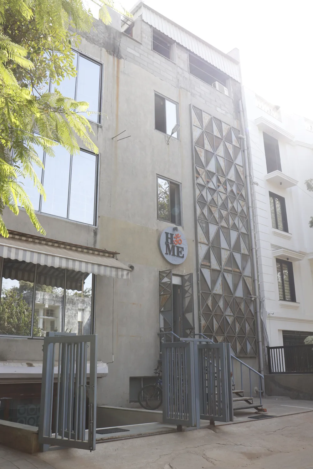 The HॐME PG building in Bodakdev, Ahmedabad — a concrete facade with a triangular steel screen and the circular HॐME logo above the door.