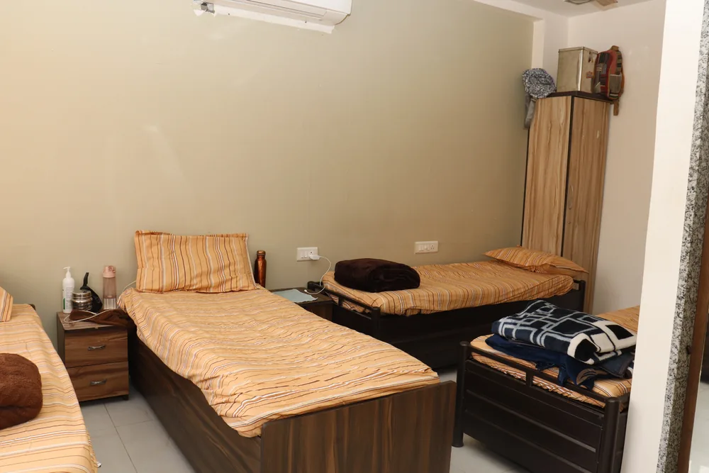 A sharing room with wooden beds, bedside tables, a wardrobe and a wall-mounted air conditioner.